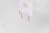 A pair of pearl earrings with silver accents, displayed against a branded background.