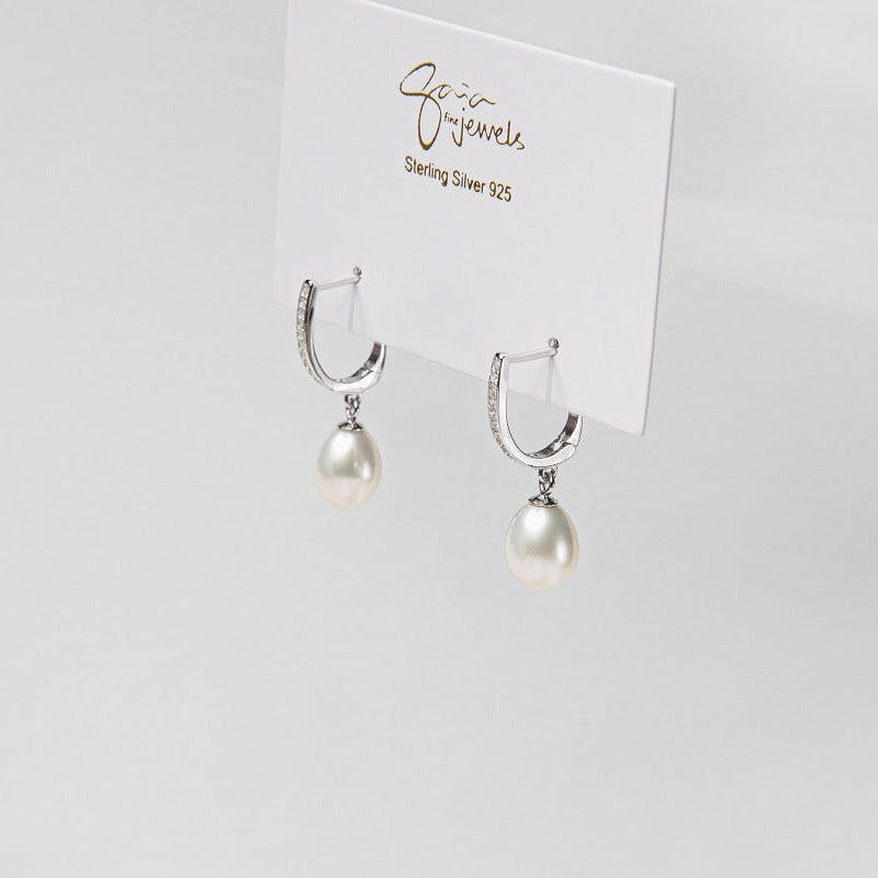 A pair of pearl earrings with silver accents, displayed against a branded background.