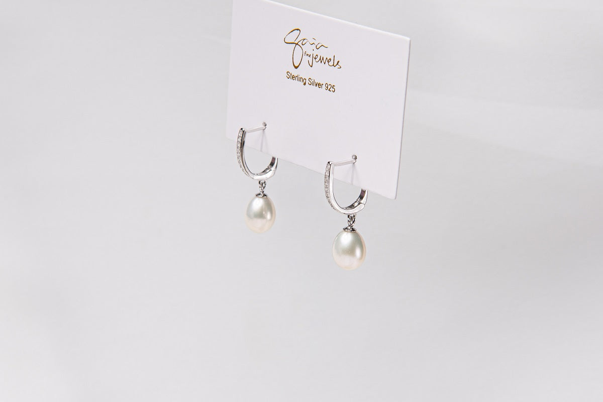 A pair of pearl earrings with silver accents, displayed against a branded background.