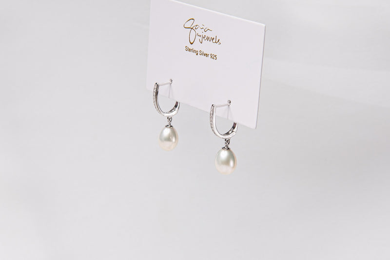 A pair of pearl earrings with silver accents, displayed against a branded background.
