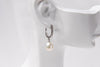 A silver earring featureing cubic zirconias and a white pearl displayed on a white mannequin head