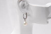 A silver earring featureing cubic zirconias and a white pearl displayed on a white mannequin head