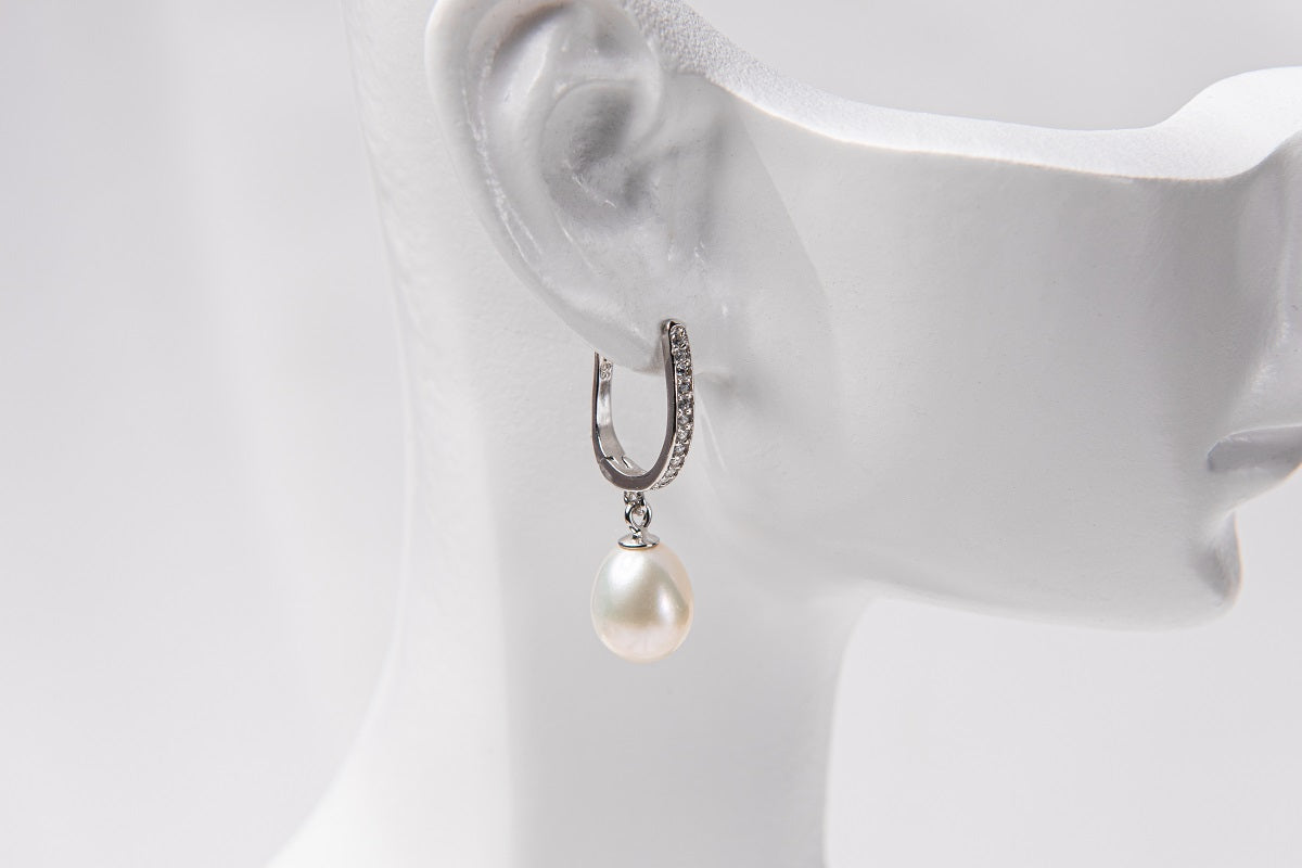 A silver earring featureing cubic zirconias and a white pearl displayed on a white mannequin head