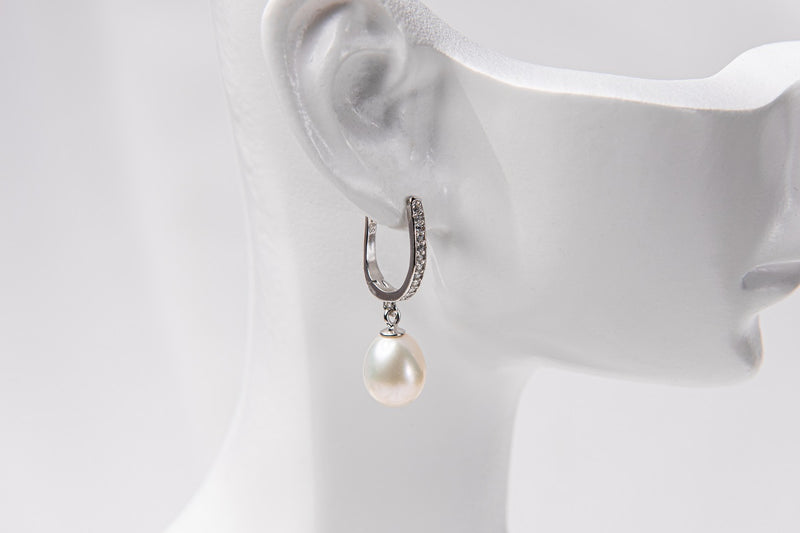 A silver earring featureing cubic zirconias and a white pearl displayed on a white mannequin head