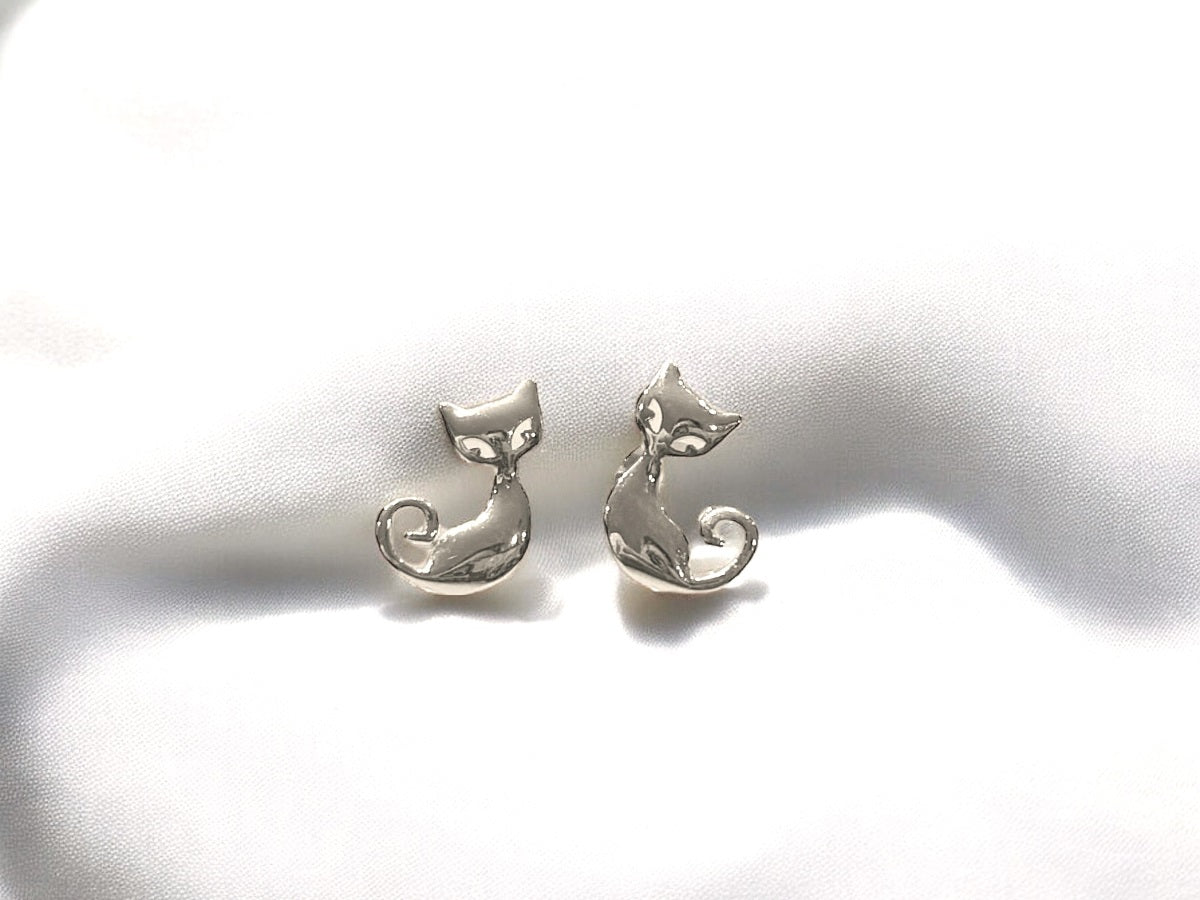 A pair of silver stud earrings featuring a cat design on the back, placed on a white fabric surface.