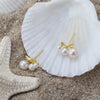 Pearl earrings with gold accents on a seashell and sand background