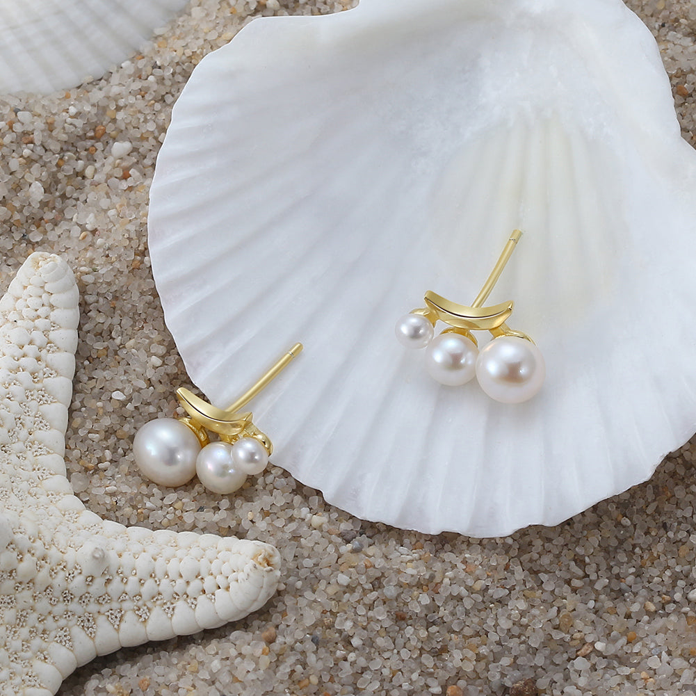 Pearl earrings with gold accents on a seashell and sand background