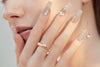 Close up of a woman wearing a gold and pearl ring with mtaching nails and earrings.