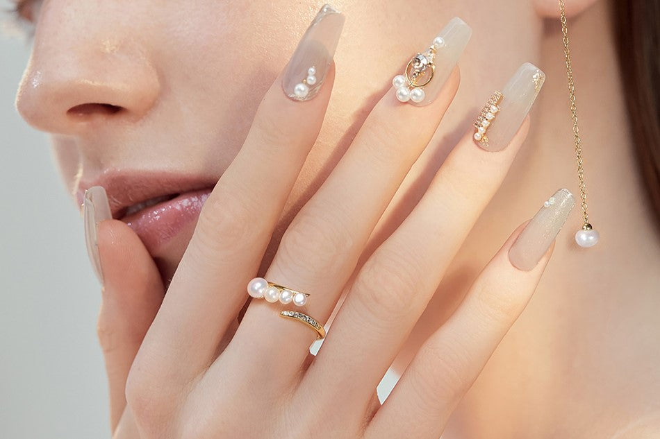 Close up of a woman wearing a gold and pearl ring with mtaching nails and earrings.