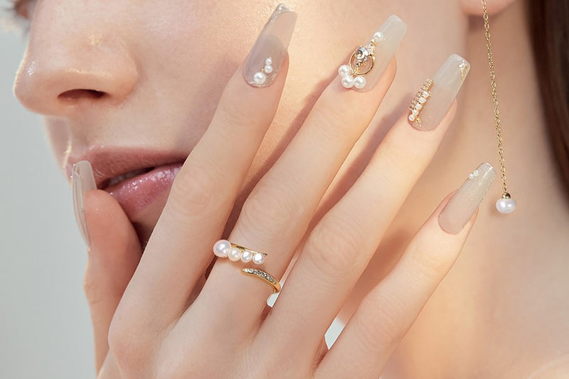 Close up of a woman wearing a gold and pearl ring with mtaching nails and earrings.