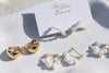 Gold and pearl hoop earrings on a white surface with a branded card.