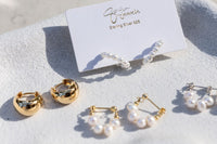 Gold and pearl hoop earrings on a white surface with a branded card.