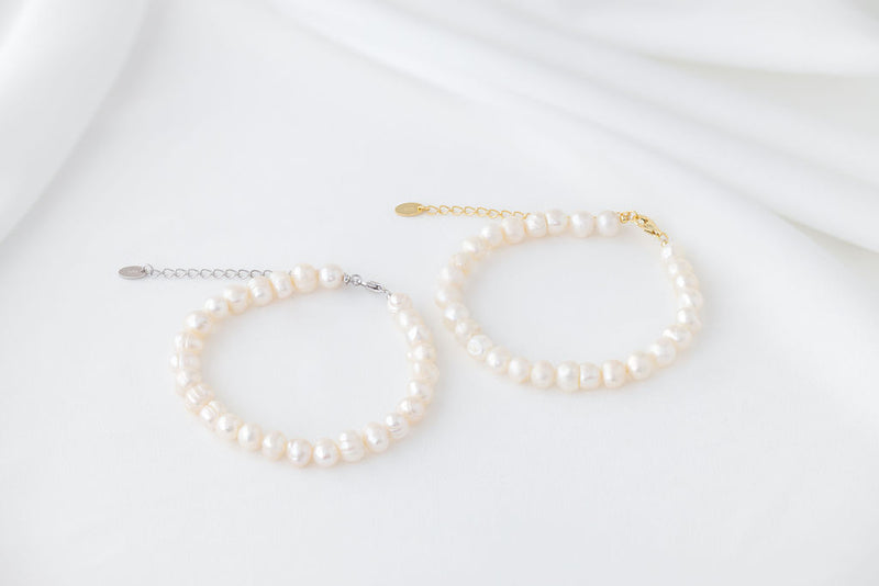 Two bracelets featureing white pearls. One with a gold chain and one with a silver chain. Displayed on a white background