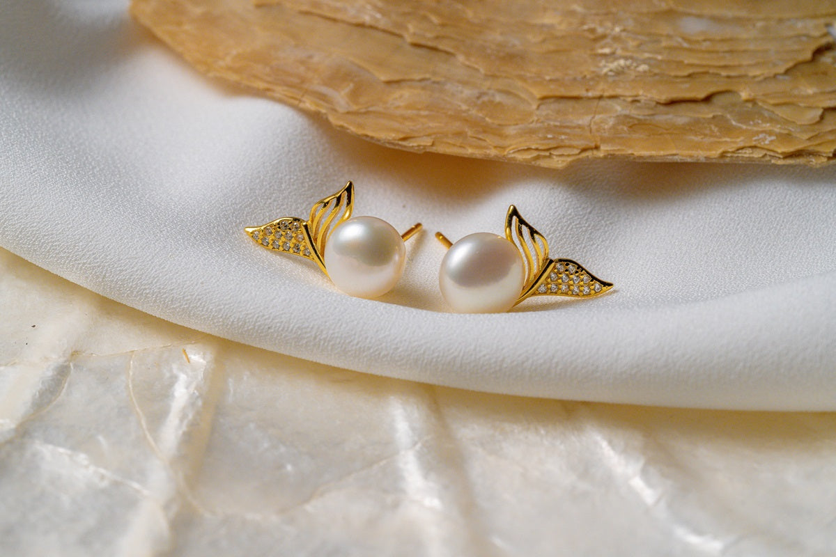 A pair of pearl earrings with butterfly backs on a white silky surface, possibly a part of a wedding dress or a bridal accessory.