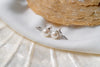 A pair of pearl earrings with butterfly backs on a white silky surface, possibly a part of a wedding dress or a bridal accessory.
