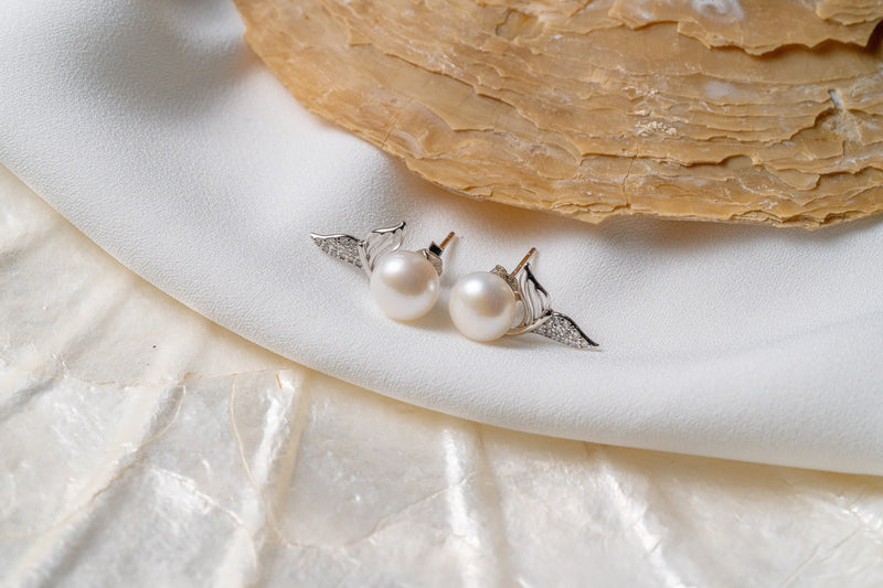 A pair of pearl earrings with butterfly backs on a white silky surface, possibly a part of a wedding dress or a bridal accessory.