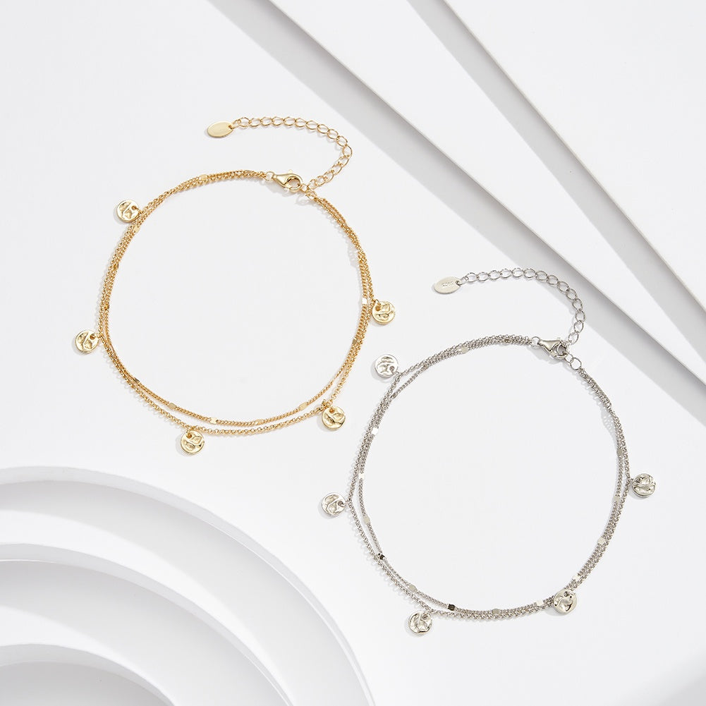 Two ankle bracelets, one Silver and one gold vermeil, each with small circular pendants engraved with a moon design, displayed against a neutral background.