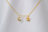A gold-colored necklace with two blue and clear cubic zirconia pendants shaped as moons and stars, displayed on a white fabric background.