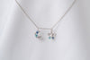 A silver necklace with two blue and clear cubic zirconia pendants shaped as moons and stars, displayed on a white fabric background.