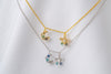 A gold-colored necklace and a silver necklace with two blue and clear cubic zirconia pendants shaped as moons and stars, displayed on a white fabric background.