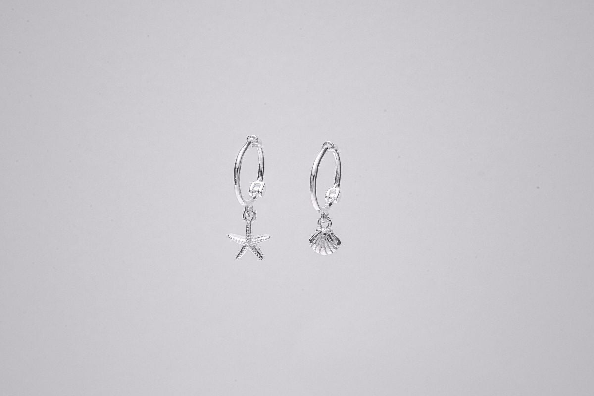 A pair of Silver hoop earrings with a starfish and shell dangle, displayed against a plain background.