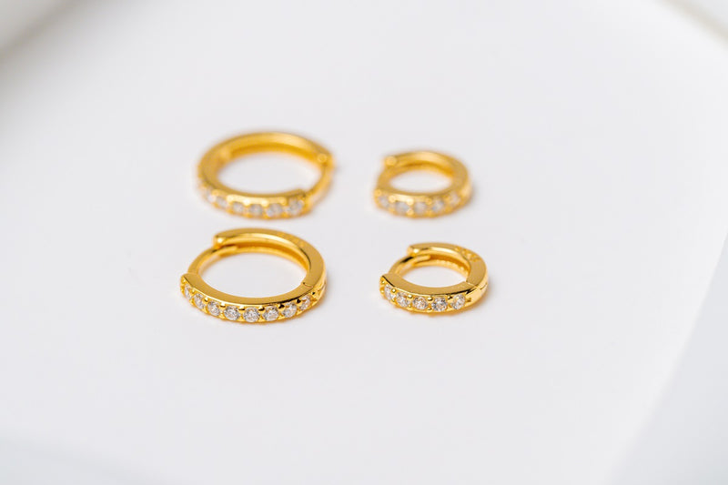 A set of gold vermeil hoop earrings with cubic zirconia accents placed on a white surface.