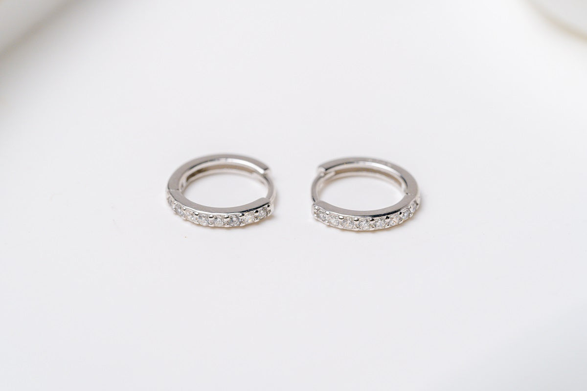 A set of Silver hoop earrings with cubic zirconia accents placed on a white surface.