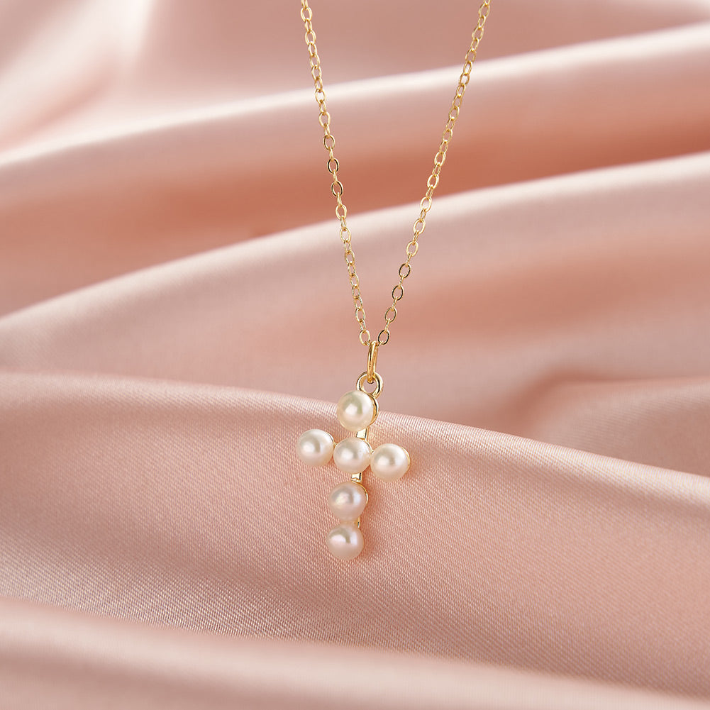 Pearl cross necklace on a gold chain against a pink fabric background