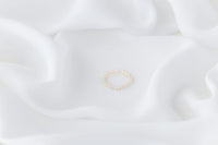 A white, baroque-shaped pearl ring with a gold band, displayed on a white fabric surface.