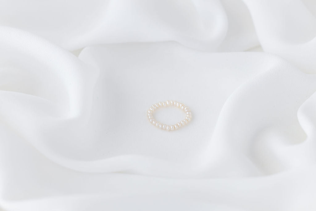 A white, baroque-shaped pearl ring with a gold band, displayed on a white fabric surface.