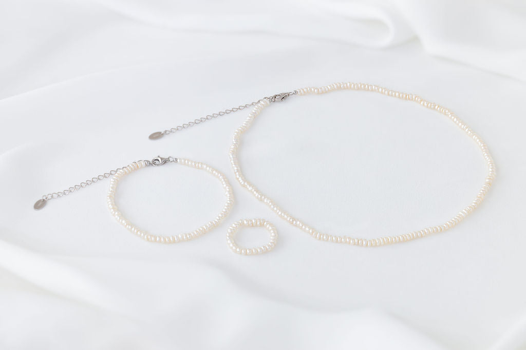 A set of elegant pearl jewellery, ring, necklace and bracelet all matching on a white background.