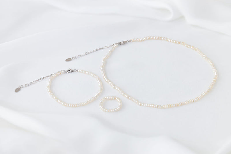 A set of elegant pearl jewellery, ring, necklace and bracelet all matching on a white background.