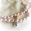 Two pearl necklaces with heart-shaped charms on a light pink fabric background