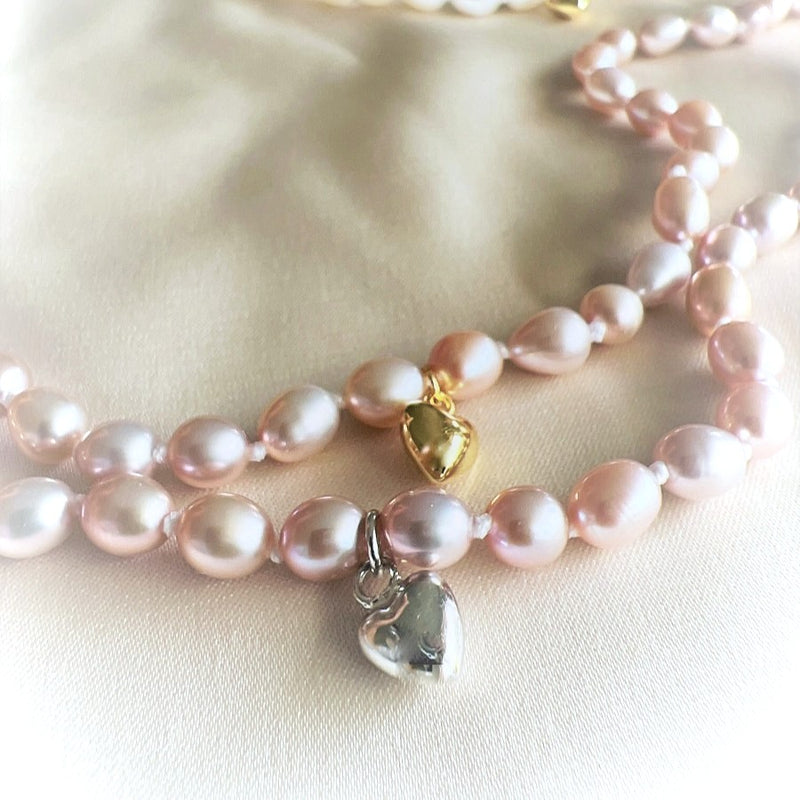 Two pearl necklaces with heart-shaped charms on a light pink fabric background