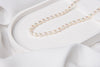 A white pearl choker necklace with a sterling silver chain, displayed on a white cushion next to a white fabric.