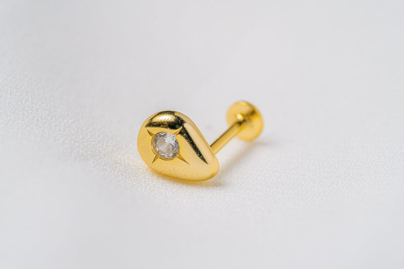 A gold raindrop shaped stud earring on a white background