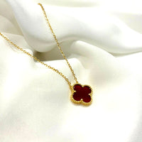 Gold necklace with a red clover pendant on a white fabric background
