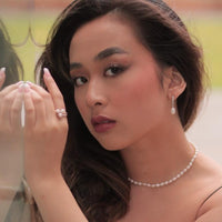 Woman wearing a pearl necklace and earrings, holding a ring with a blurred background