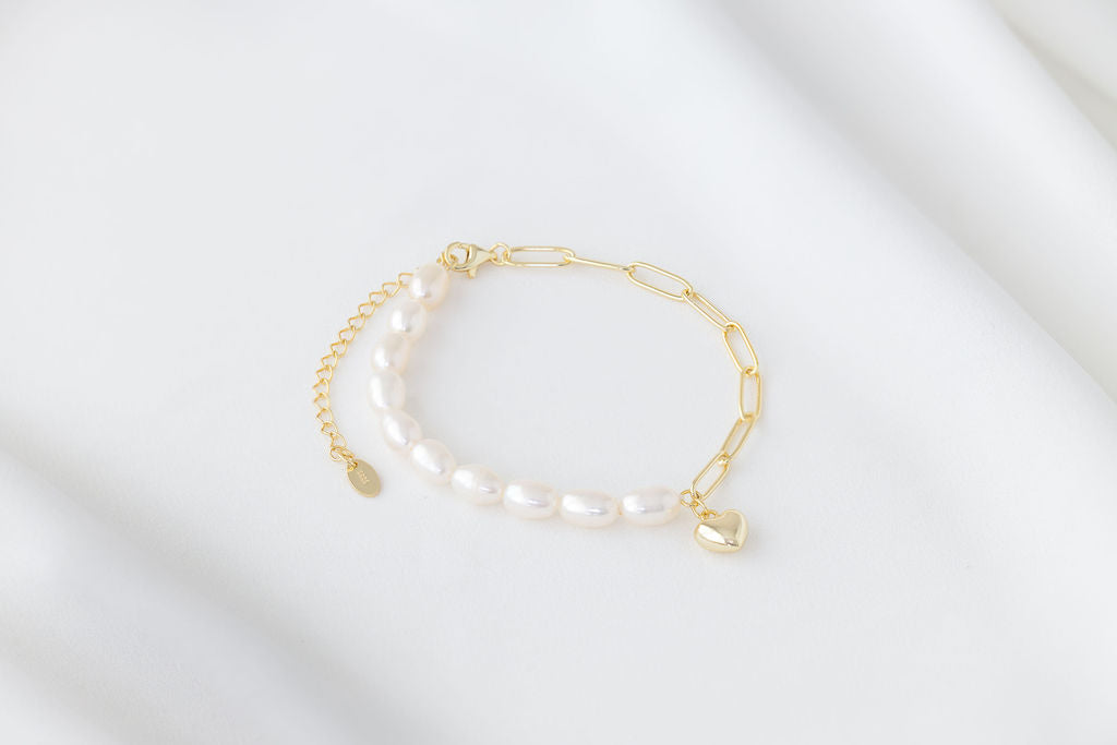 Pearl bracelet with a gold heart charm on a white background