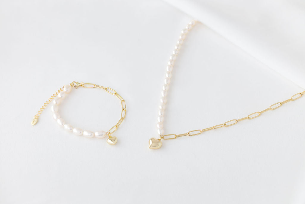 Pearl bracelet  and matching necklace with a gold heart charm on a white background