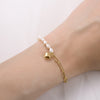 Gold bracelet with heart and paperclip charm on a wrist against a light background