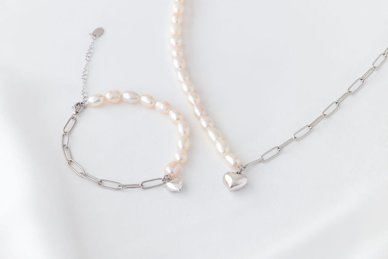 Pearl bracelet and matching necklace with a silver heart charm on a white background