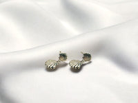 A pair of silver stud earrings with sea shell designs on a white silky surface.