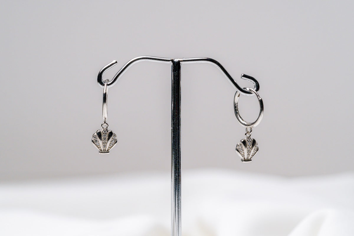 This image displays a pair of elegant shell-themed earrings, referred to as "Shell Huggies." The earrings feature a detailed and textured design that mimics the natural pattern of a shell, with a golden finish that adds a touch of sophistication.