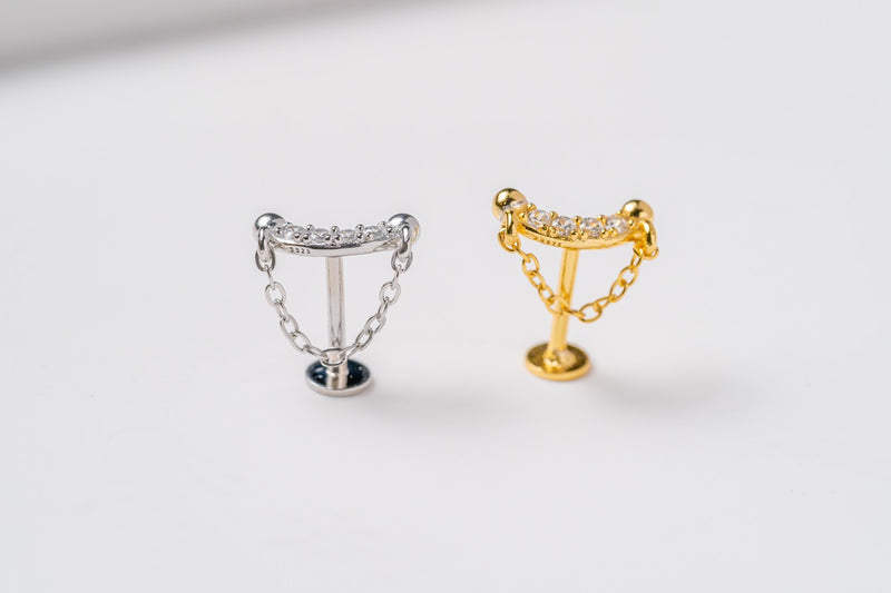 A silver stud earring and a gold stud earring featuring cubic zirconias and a fine chain design to look like a shield both on a white background