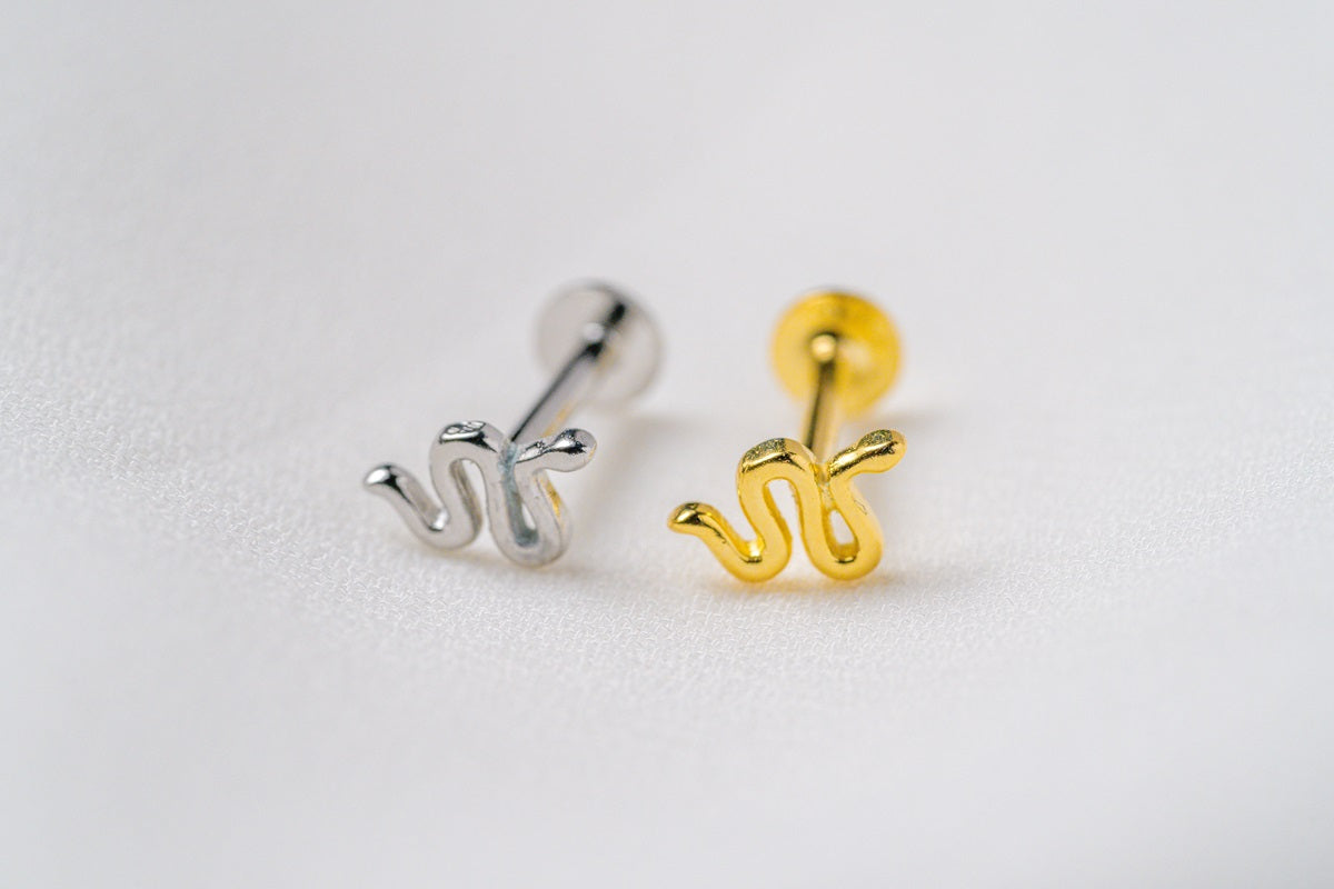 A silver and a gold shaped earring on a white background