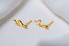 A pair of gold stud earrings with a snake-like pattern, displayed against a white background.