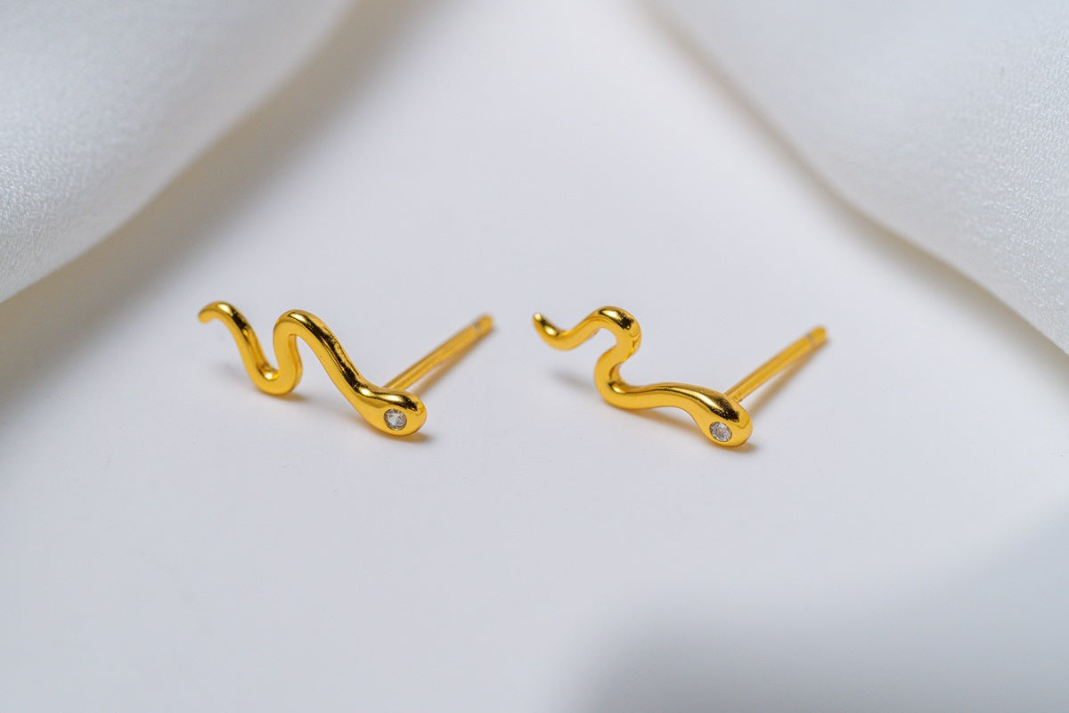 A pair of gold stud earrings with a snake-like pattern, displayed against a white background.