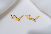 A pair of gold stud earrings with a snake-like pattern, displayed against a white background.