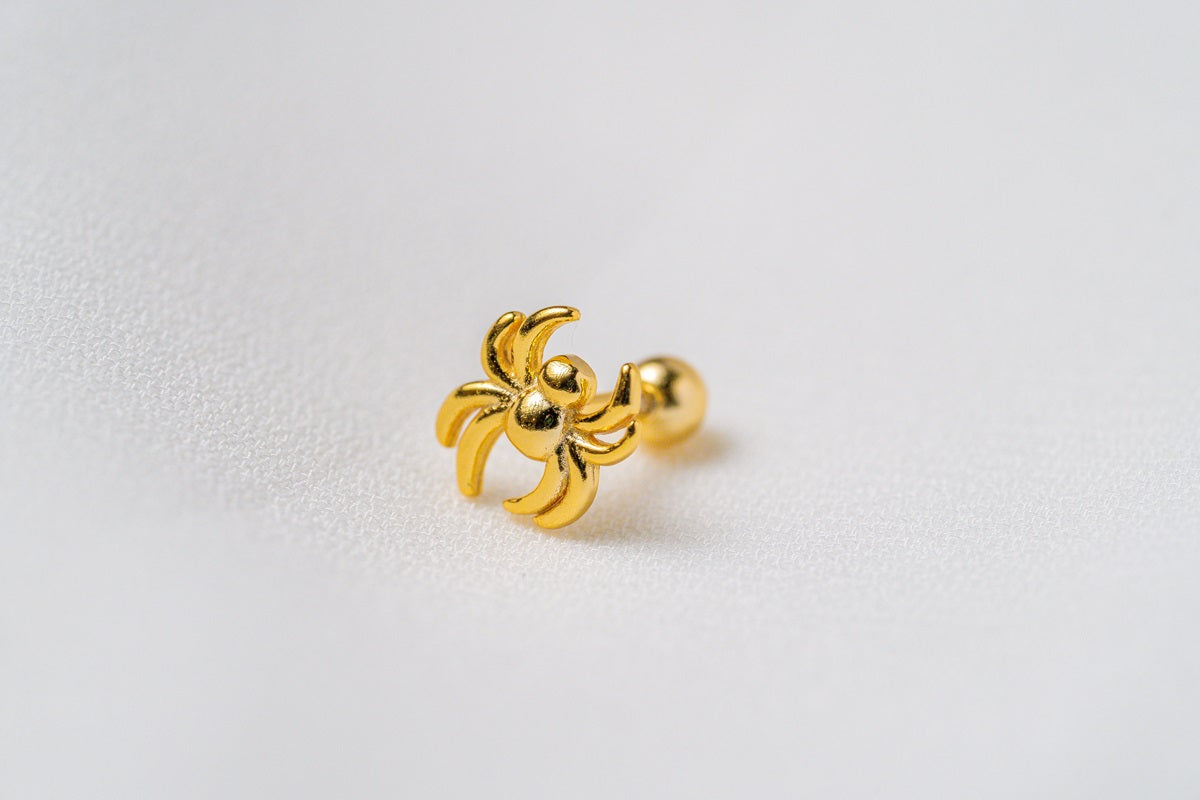A gold-colored spider-shaped piercing jewelry with a textured surface on a white background.